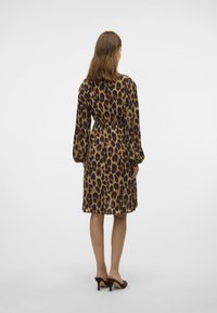 Vestido de leopardo con mangas largas y cintura elástica, que presenta una silueta holgada. La tela tiene una textura suave y se lleva con tacones.