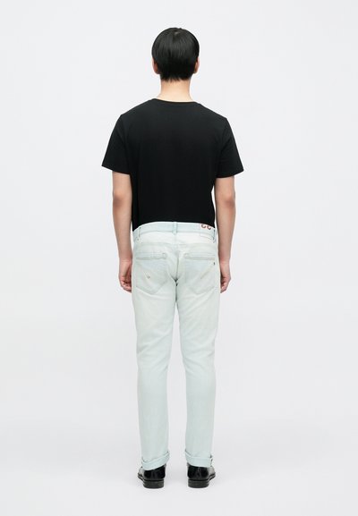 Μαύρο κοντομάνικο μπλουζάκι, ανοιχτό μπλε τζιν με δύο πίσω τσέπες, γυρισμένα μανίκια και σκούρα παπούτσια, ορατά από πίσω.