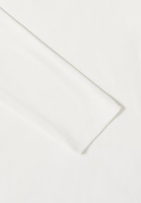 Tissu blanc côtelé montrant une extrémité de manche, présentant un bord net sans ornements ni motifs, avec une texture lisse.