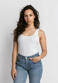 Witte tanktop met een ronde halslijn, gecombineerd met hooggetailleerde blauwe denim jeans. De stof lijkt glad met een aansluitend ontwerp.