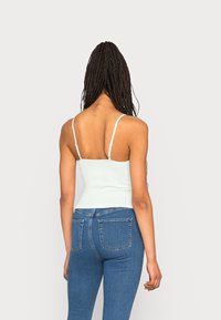Top de malha canelada em verde-claro com alças finas ajustáveis, combinado com jeans azul de cintura média com bolsos traseiros.