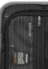 Interno di un bagaglio in tessuto nero con strisce bianche verticali, numerosi scomparti con zip e etichetta del marchio ben in evidenza.