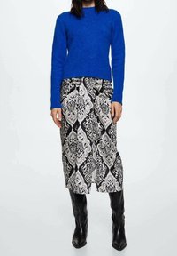 Un pull bleu royal et une longue jupe noire avec un motif damassé blanc et gris élaboré; associés à des bottes noires au genou.
