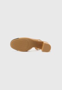 Scarpa con tacco color beige, dalla texture liscia, con punta arrotondata e suola in gomma con motivo. Il tacco è corto e di tipo block per garantire stabilità.