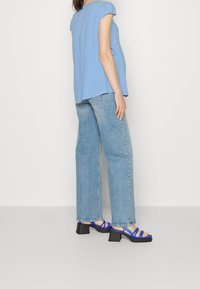 Světle modrý top s krátkým rukávem a rozšířeným lemem, kombinovaný s vysokým pasem světle modrých džínů a modrými sandály na block podpatku se šněrováním.