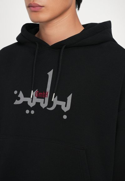 Felpa nera con cappuccio e cordino, caratterizzata da un logo grigio in evidenza e testo rosso a contrasto. Tessuto morbido, vestibilità casual, tasca a marsupio.