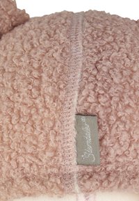 Light pink, textured cushion with curly fabric, displaying a stitched seam and a small gray label on the side. Soft and plush appearance.