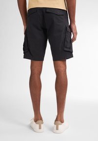 Sorte cargo shorts med flere sidelommer, lavet af bomuldsstof, og en afslappet pasform. Kombineret med hvide sneakers og en lysefarvet T-shirt.