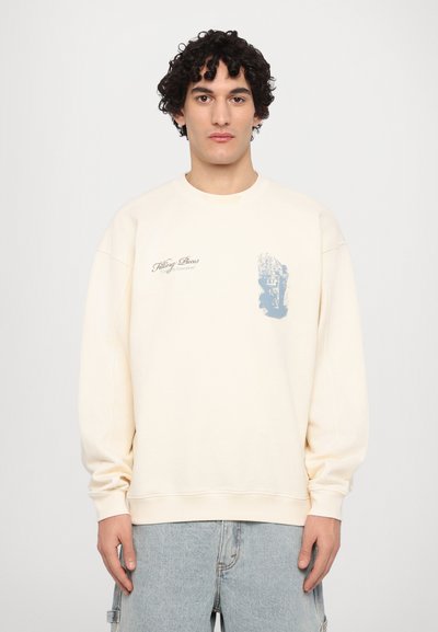 Cremefarbener Pullover mit langen Ärmeln, der auf der Vorderseite ein blaues Grafikdesign und Text aufweist. Weicher Stoff mit lockerem Schnitt.