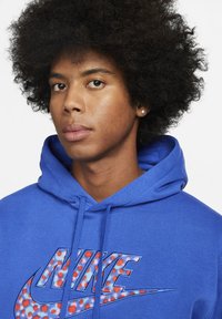 Blå hoodie lavet af bomuld, med et fremtrædende flerfarvet Nike-logo med et prikket mønster. Hætte med snore, tekstureret stof.