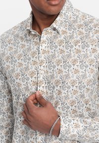 Witte blouse met lange mouwen en een bloemenpatroon in grijs, geel en bruin. Voorzien van een button-down kraag en knopen aan de voorkant. Structuurstof.