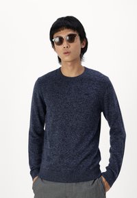 Suéter azul marino de punto texturizado con cuello redondo y puños acanalados, combinado con gafas de sol oscuras de montura redonda.