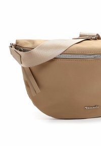 Bolso bandolera beige con cremallera plateada, correa ancha de tela ajustable y pequeño logo metálico en el frente, mostrado sobre un fondo blanco.