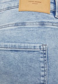 Jeans de mezclilla azul claro con un bolsillo trasero y una etiqueta de cuero con "VERO MODA" y "DENIM" en relieve en marrón.