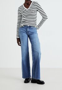 Striped long-sleeve V-neck top in black and white, paired with light blue wide-leg jeans. Black chunky shoes complete the look.