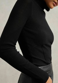 Schwarzes langärmliges Rollkragenoberteil aus strukturiertem Strickstoff, mit tailliertem Design und Nahtdetails an den Ärmeln und dem Rumpf.