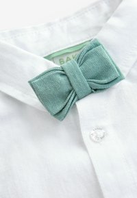 White shirt collar with a textured light green bow tie. Features a button near the collar with "BAKER" engraved. Smooth fabric finish.