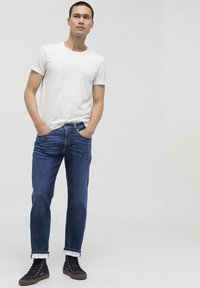 Camiseta blanca de cuello redondo, jeans de mezclilla azul con puños enrollados y zapatillas altas negras. Tejido suave, corte ajustado y detalles de costura sutiles.