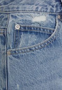 Jeans de ganga azul clara com áreas desgastadas, um bolso frontal, metais prateados e costura em contraste ao longo das costuras.