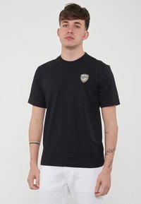 Maglietta nera in cotone con maniche corte, scollatura rotonda e un logo sulla parte sinistra del petto. Design semplice, senza motivi o accenti visibili.