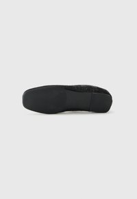 Chaussure plate noire avec un dessus texturé, dotée d'un bout rond lisse et d'une semelle en caoutchouc noir flexible. Design global minimaliste.