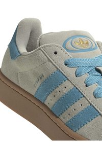Sneaker in suede grigio e azzurro chiaro, con tre strisce, dettagli testurizzati, lacci rotondi e un logo dorato sulla linguetta.