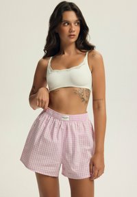 Jasnoróżowe i białe szorty w kratkę z elastycznym pasem i metką. Połączone z białym stanikiem typu bralette z koronkowymi detalami.
