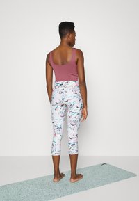 Top de tanque ajustado em bordô e leggings capri estampadas com desenhos florais em tons pastel, acompanhados de um tapete de yoga cinza claro.
