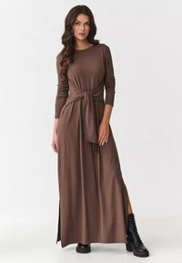 Brązowa sukienka maxi z długim rękawem i zawiązywaną talią, z rozcięciem z przodu. Wykonana z miękkiego materiału, ma luźny krój i gładką strukturę.