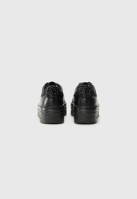 Black platform sneakers with smooth leather material, rounded toe, textured rear panel, and decorative black gems on the back.