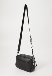 Borsa a tracolla nera in pelle con superficie testurizzata, compartimenti con doppia zip, tracolla regolabile e tasca anteriore.