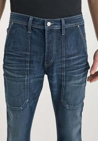 Jeans de denim azul oscuro con un corte relajado, que cuentan con múltiples bolsillos, un desgaste sutil y detalles de costura en contraste.