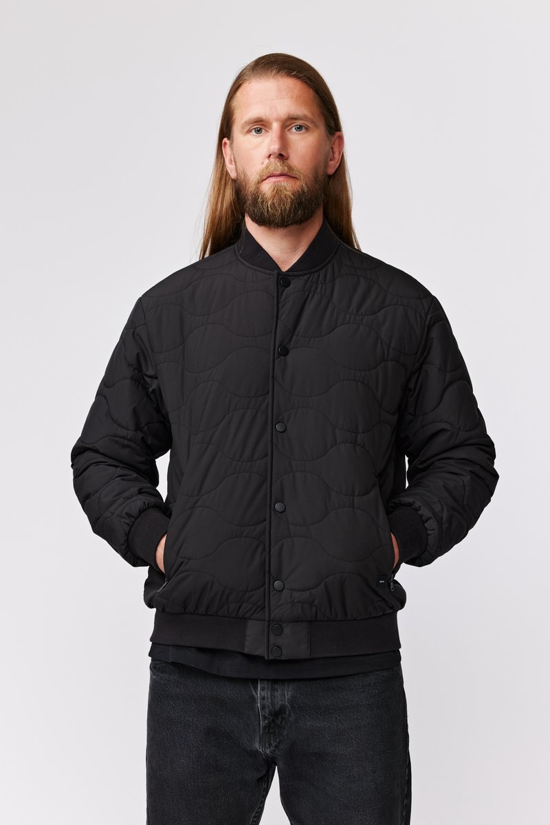Veste bomber matelassée noire avec col rond, boutons-pression et poignets côtelés. Présente une texture douce et des accents de design minimalistes.