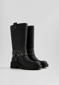 Botas de cuero negro con diseño alto, que cuentan con dos hebillas con detalles metálicos, puntera redonda y tacón grueso. Acabado texturizado con costuras grises.