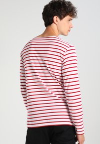 Camicia a manica lunga a righe rosse e bianche, realizzata in cotone leggero. Presenta una vestibilità rilassata e un collo a giro.