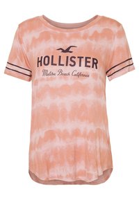 Short-sleeve t-shirt in light peach tie-dye pattern; features black "Hollister" logo and "Malibu Beach California" text; rounded neckline.