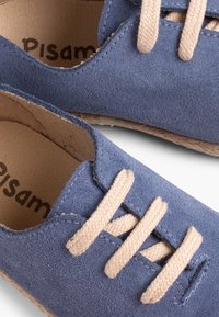 Scarpe blu scamosciate con lacci beige, caratterizzate da una texture morbida e un design arrotondato. Le solette mostrano il nome del marchio "Pisamon" in un colore chiaro.