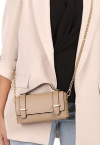 Beige nepleer handtas met zwarte accenten, rechthoekige vorm, gouden hardware, bovenhandvat en afneembare kettingriem.