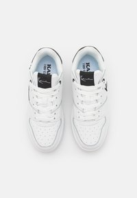 Hvide sneakers med sorte accenter, fremstillet af læder og mesh, med en perforeret tåboks, snørebånd og et logo på tungen.
