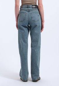 Light blue high-waisted jeans with a relaxed fit. Features two back pockets and a black brand label on the waistband. Woven denim texture.