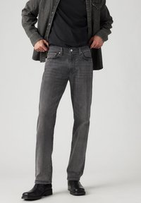 Šedé džíny z denimu s rovnými nohavicemi, pět kapsami a kontrastním prošíváním, spárované s černými koženými botami a tmavým tričkem.