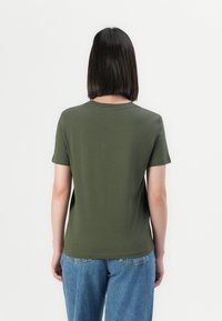 T-shirt verde oliva a maniche corte con scollatura rotonda, realizzato in tessuto morbido, abbinato a jeans in denim blu chiaro. Design semplice, senza grafiche.