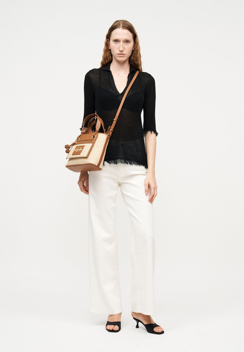 Γυναίκα που φοράει διαφανές μαύρο τοπ, λευκό παντελόνι με φαρδιά μπατζάκια, μαύρα ψηλοτάκουνα σανδάλια, κρατώντας μια τσάντα σε ταμπά και μπεζ με ιμάντα ώμου.