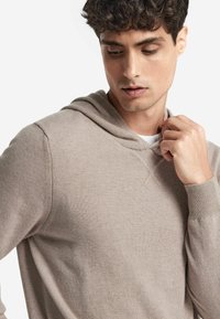 Beige Kapuzenpullover aus weichem Stoff, mit lockerer Passform, gerippten Bündchen und einem einfachen Steppdetail am Ausschnitt.