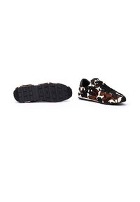 Zapatillas con estampado de cuero de vaca en marrón y blanco, con suela de goma negra, diseño con cordones y superficie texturizada para un mejor agarre.