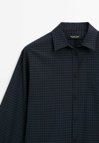Chemise à manches longues à carreaux bleu foncé et noir, boutonnée, avec col et poche poitrine, vue de face sur fond blanc.