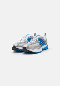 Chaussures de sport avec une tige en maille argentée et des accents bleus, dotées de lacets blancs et d'une semelle en caoutchouc noir avec un amorti bleu.