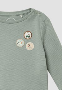 Lichtgroen lange mouwen shirt met ronde hals, voorzien van drie geborduurde patches: een koe, een tractor en een ezel. Twee knopen op de schouder.