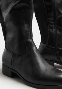 Czarne skórzane za kolano botki o gładkim wykończeniu, z okrągłym noskiem, słupkowym obcasem i bocznym zamkiem błyskawicznym ułatwiającym zakładanie.