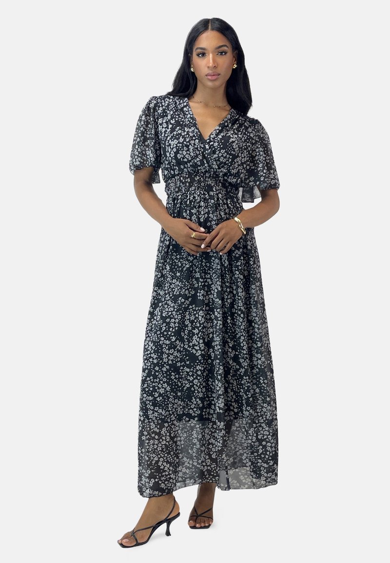 Schwarzes Blumen-Maxikleid mit kurzen Puffärmeln, taillierter Detail, transparenter Stoff und verstreuten weißen Blumenmustern. Verstellbarer Ausschnitt.